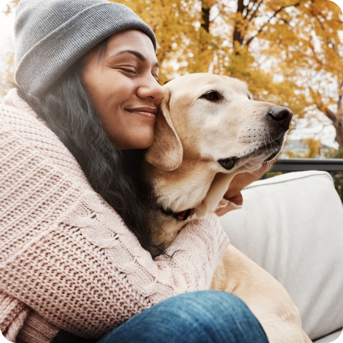 Woman hugging a Labrador retriever outside in autumn.