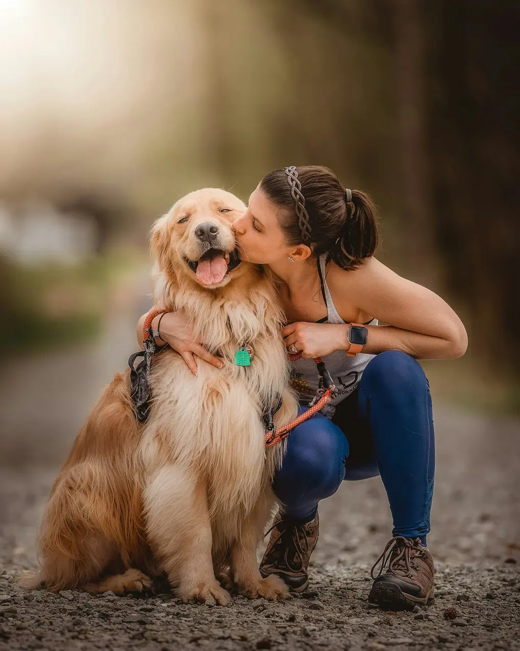 A woman kisses a happy Golden Retriever outdoors on a path.